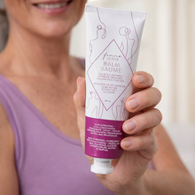 Load image into Gallery viewer, A woman holding a tube of FemmeSense Vulva Balm with a blurred background
